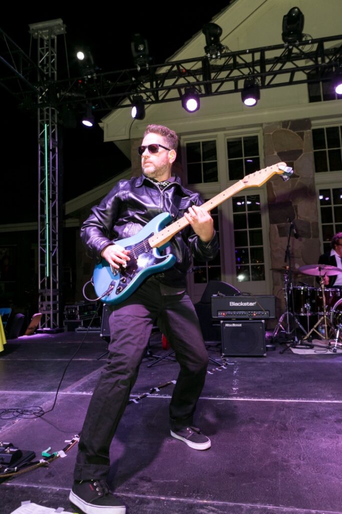 A man in black jacket playing guitar on stage.